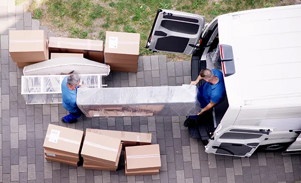 Équipe SereniMove chargeant des meubles protégés avec soin Deux déménageurs professionnels chargeant un meuble emballé dans une camionnette de déménagement