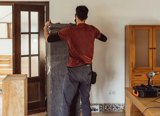Déménageur protégeant un meuble avant transport — SereniMove Déménageur emballant un meuble avec une couverture de protection avant déménagement