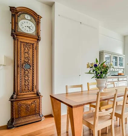 Horloge ancienne en bois sculpté dans un intérieur domestique Horloge ancienne en bois sculpté dans une salle à manger lumineuse, illustrant les biens de valeur récupérables lors d'un vide-maison